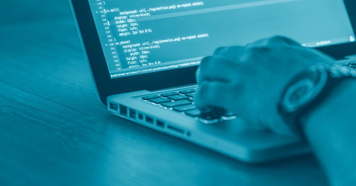 Mão digitando em notebook com linhas de código representando tratamento de dados no Power Query