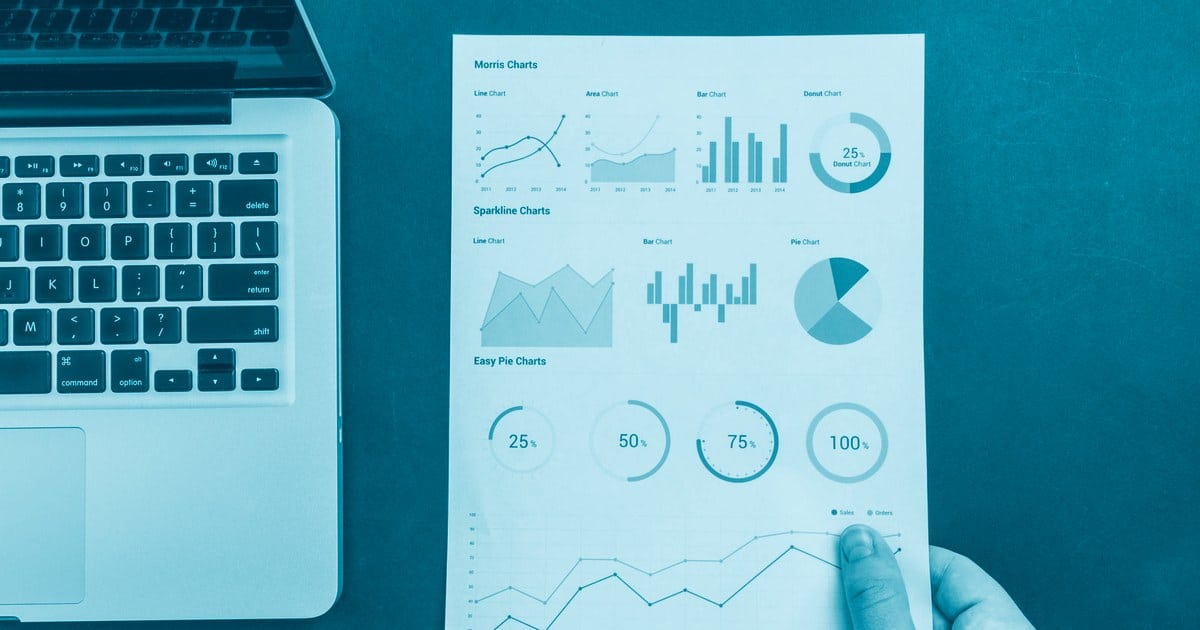 Mão segurando relatório com gráficos de dashboard ao lado de notebook, representando erros comuns em dashboards de Power BI