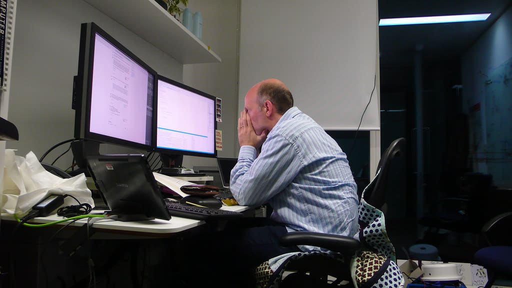 Profissional sobrecarregado analisando múltiplos monitores no escritório
